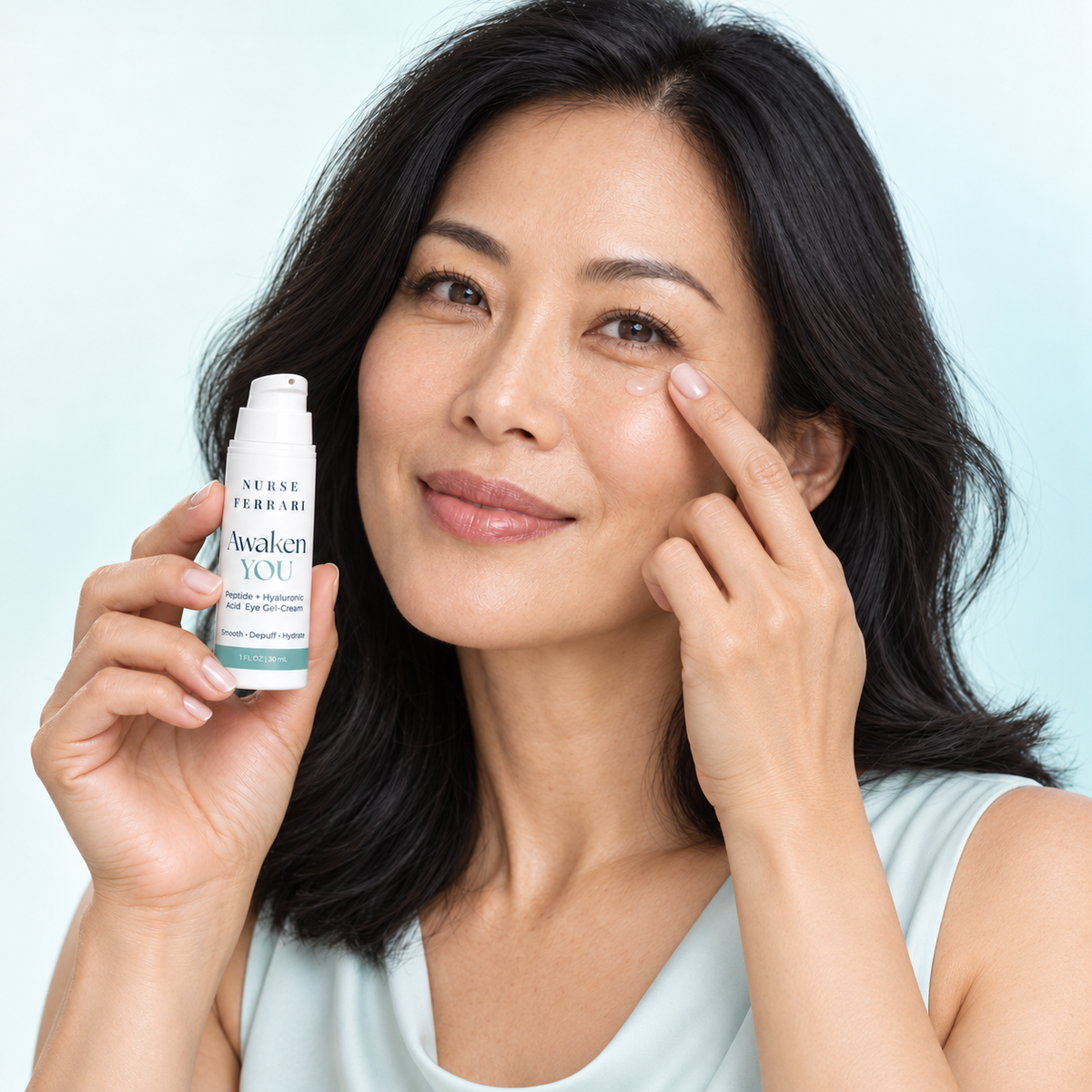 East Asian woman correctly tapping Awaken YOU gel-cream beneath her eye while holding the uncapped product
