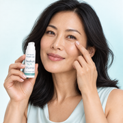 East Asian woman correctly tapping Awaken YOU gel-cream beneath her eye while holding the uncapped product
